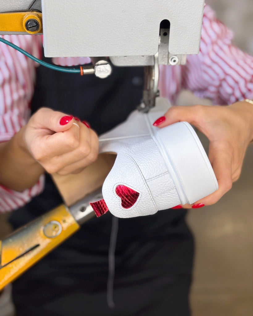 Person holding a white sneaker with red accents near a sewing machine.